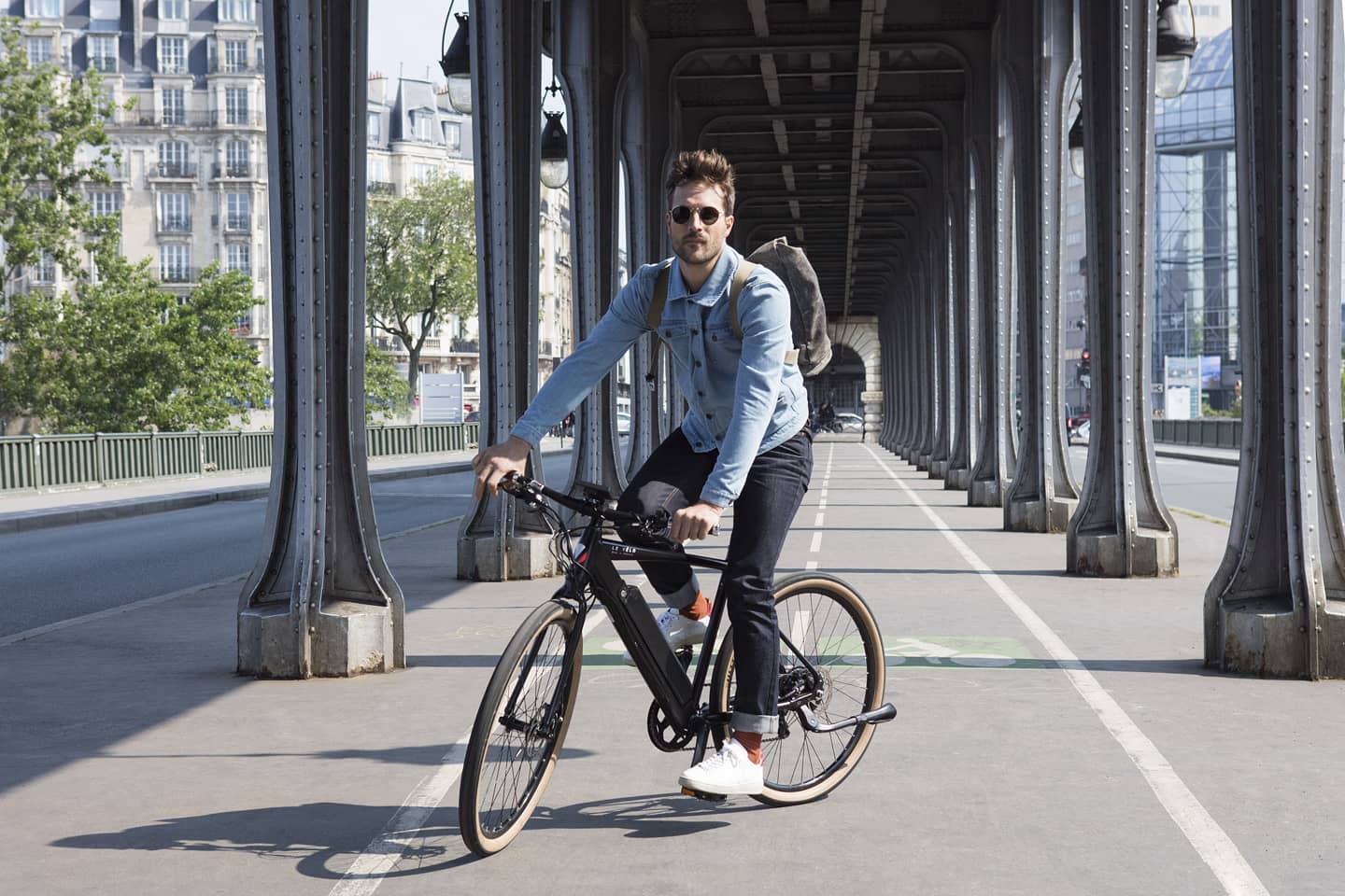 Homme à vélo sous un pont parisien.