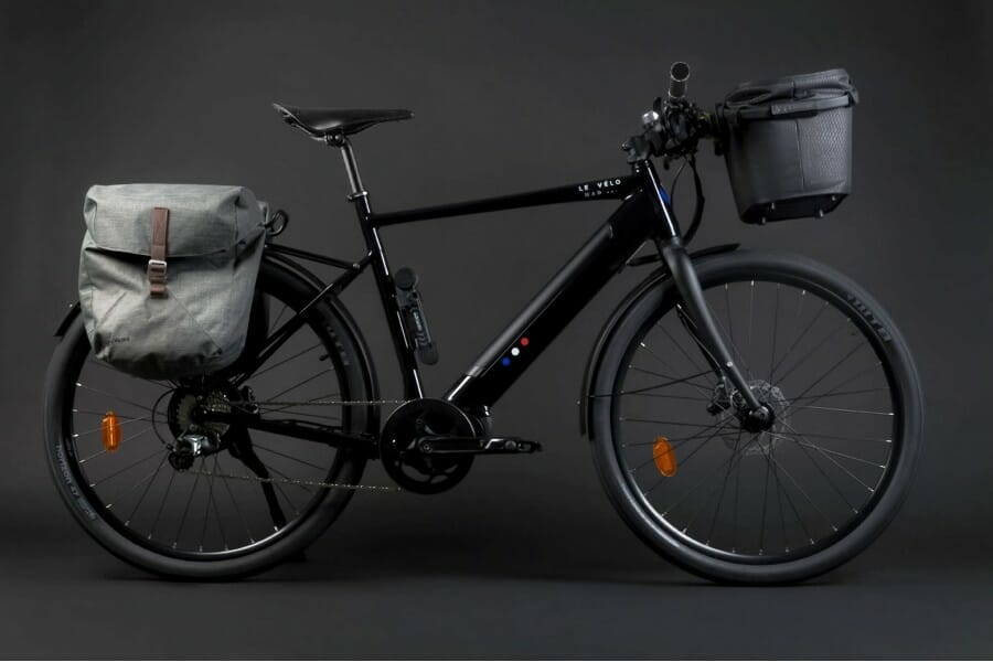 Vélo électrique noir équipé de sacoches, sur fond gris.